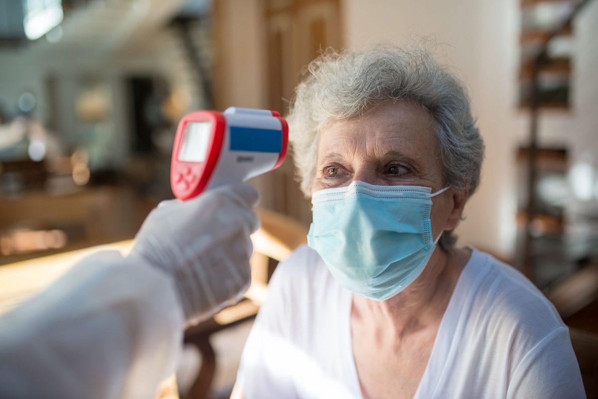 Senior woman in a mask having her temperature checked, a reminder of covid-19 in aged care facilities